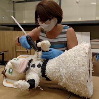 Image of Elena Baca, visual arts educator, fixing a piñata with a hot glue gun.