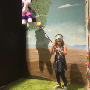 a young girl wearing a mask over her eyes, preparing to hit a piñata